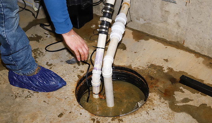 Sump pump in flooded basement being repaired by plumber.